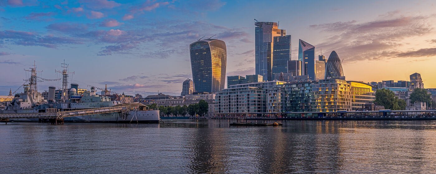 The City of London skyline across the Thames at sunrise, with HMS Belfast moored in the foreground