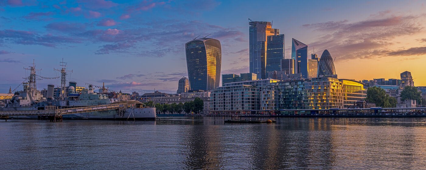 The City of London skyline across the Thames at sunrise, with HMS Belfast moored in the foreground